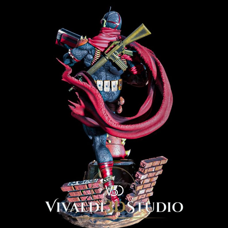 Peut inclure: Une figurine d&eacute;taill&eacute;e d'un personnage &agrave; la peau sombre avec une armure textur&eacute;e, portant une cape rouge flottante et un fusil dor&eacute;. La figurine repose sur une base en briques cass&eacute;es avec le texte VIVALDI STUDIO inscrit en bas.