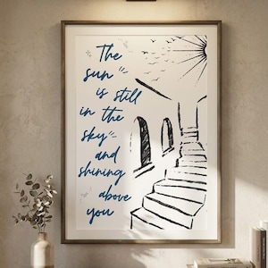 May include: A framed wall art print featuring a black and white line drawing of a staircase leading upwards towards a sun and birds, with the blue text "The sun is still in the sky and shining above you" printed on the left side of the white background.