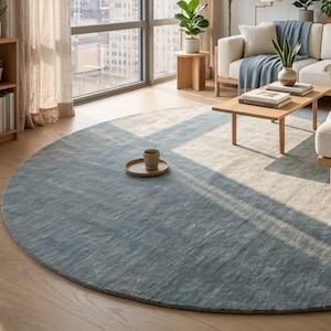 May include: A large, circular area rug featuring a two-tone design with a soft blue section and a neutral beige section. The rug has a low-pile, textured surface and is positioned on a light-colored wooden floor, creating a focal point in the room.