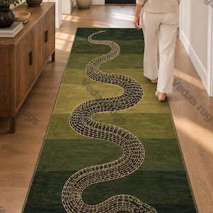 Puede incluir: Una alfombra de pasillo rectangular larga con un degradado de tonos verdes de claro a oscuro. La alfombra muestra un gráfico grande de una serpiente sinuosa con un patrón de escamas detallado delineado en oro a lo largo de toda la superficie.