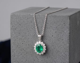May include: A silver necklace featuring an oval-cut green gemstone pendant surrounded by a halo of small, clear, round-cut stones. The pendant is suspended from a delicate silver chain with a classic link design, creating a refined jewelry piece.