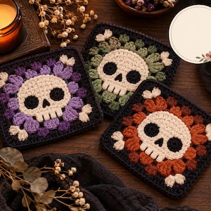 May include: Three square crochet coasters featuring a central off-white skull motif surrounded by petals in purple, sage green, and burnt orange. Each coaster has a dark border and small white corner accents, showcasing detailed yarn work.