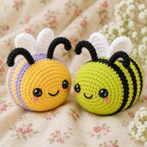 Puede incluir: Dos peluches de abeja tejidos a ganchillo con alas blancas y antenas negras. Una abeja tiene rayas amarillas y moradas, mientras que la otra tiene rayas verde lima y negras. Ambas tienen ojos de seguridad negros, sonrisas bordadas y mejillas rosadas.