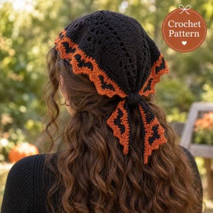 Pode incluir: Um lenço de crochê preto com uma borda laranja com padrão de morcegos. A cobertura triangular para a cabeça amarra-se na parte de trás e inclui um gráfico circular no canto com o texto Crochet Pattern e um ícone de coração.