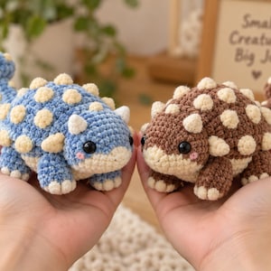 Peut inclure: Deux figurines ankylosaure au crochet, une bleue et une marron, toutes deux dotées de pointes couleur crème, d'yeux noirs ronds et de petites marques roses sur les joues. Chaque dinosaure a un corps texturé et une queue arrondie.