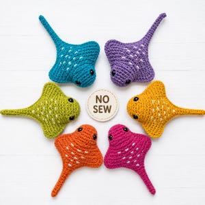 May include: Five crocheted stingray toys in teal, purple, lime green, yellow, orange, and magenta, arranged in a circle around a small circular tag that reads NO SEW. Each stingray features black bead eyes and white stitched accents on the back.