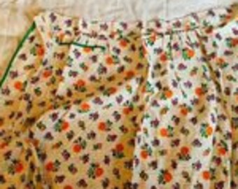 May include: A white apron with a floral print in shades of orange, purple, and green. The apron has green trim and ties.
