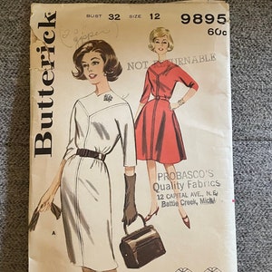 Op de afbeelding: Vintage naaipatroon voor een jurk, maat 12, borstomvang 81 cm. Het patroon is voor een witte jurk met een zwarte riem en een rode jurk met een witte kraag. Het patroon is van Butterick en is gemarkeerd met "Niet Retourneerbaar".