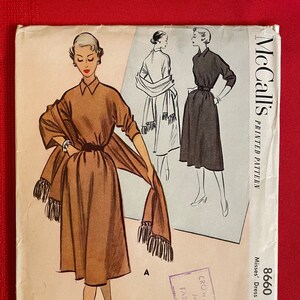Puede incluir: Un patrón de costura vintage de McCall's para un vestido y una estola. El patrón es para la talla 10, busto 73 cm, y cuesta 35 centavos. El patrón presenta un vestido marrón con un cuello blanco y una estola marrón a juego con flecos.