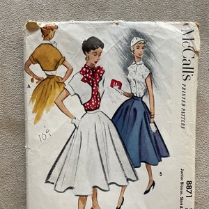 Puede incluir: Patrón de costura vintage McCall's para una blusa, falda y bolero junior. El patrón es para la talla 15, busto 84-89 cm. El patrón muestra tres estilos diferentes del atuendo, con una blusa y falda blancas, una blusa roja y blanca con una falda blanca y una blusa blanca con una falda azul.