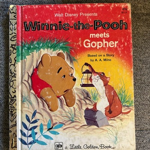Könnte beinhalten: Ein Vintage-Cover eines Little Golden Books, das Winnie Puuh zeigt, wie er Gopher trifft. Das Cover ist rot und gelb mit Illustrationen von Winnie Puuh und Gopher in einer Waldlandschaft. Der Buchtitel lautet "Winnie Puuh trifft Gopher" und der Text "Basierend auf einer Geschichte von A. A. Milne" ist ebenfalls enthalten.