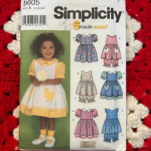 Pode incluir: Padrão de costura Simplicity 9605 para vestidos e roupas de menina. O padrão apresenta uma foto de uma menina usando um vestido amarelo e branco com uma aplicação de galinha. O padrão inclui vários modelos de vestidos.