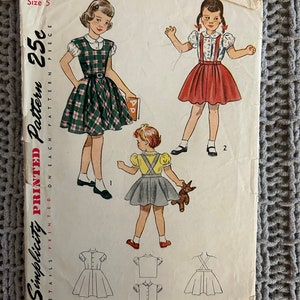 May include: Vintage Simplicity sewing pattern for a girl's dress. The pattern is for size 5 and includes a plaid dress, a red dress, and a yellow dress. The pattern is printed on a white background with black text. The pattern number is 2933 and the price is 25 cents.