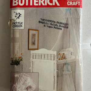 Puede incluir: Una cuna blanca con una capota blanca y una falda con volantes blancos. La cuna está decorada con un oso de peluche y un animal de peluche. El patrón es para una capota de cuna, una falda y una colcha. El patrón es de Butterick y es el número 4689.