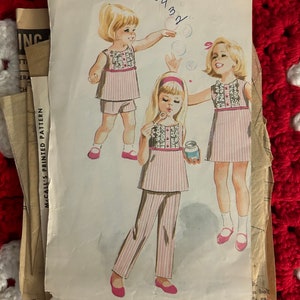 Puede incluir: Patrón de costura vintage para un conjunto de vestido y pantalones para niñas. El patrón es para las tallas 4-6 y presenta una tela a rayas rosa y blanca con un cuello con volantes. El número del patrón es 8240.