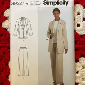Puede incluir: Patrón de costura Simplicity S9227 con blazer y pantalón. El patrón incluye un dibujo lineal del blazer y el pantalón, y una foto de una persona que lleva el conjunto. Talla EE. UU. 18-26.