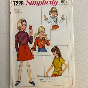 Op de afbeelding: Simplicity naaipatroon nummer 7229 voor een kinderjurk. Het patroon bevat vier verschillende stijlen: een rood-wit gestreept overhemd met lange mouwen en een rode rok, een wit blouse met gerimpelde mouwen en een rode rok, een rood-witte bloemenprint overhemd met lange mouwen en een blauwe rok, en een geel overhemd met korte mouwen en een rode rok. Het patroon is voor maat 6 en heeft een borstomvang van 61 cm.