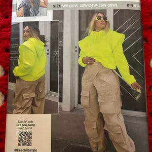 May include: Sewing pattern for a neon yellow hooded sweatshirt with ruffle detailing and beige cargo pants. The pattern is called "knowme" by mimig and is size W2 (20W-22W-24W-26W-28W).