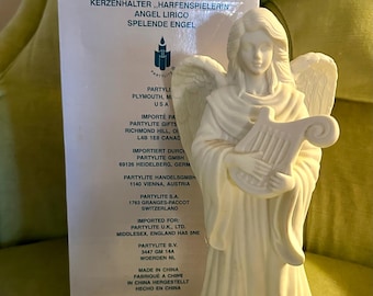 Puede incluir: Figura de ángel de porcelana blanca sosteniendo un arpa. La caja dice "Lyrical Angel" e incluye información sobre el fabricante, Partylite.