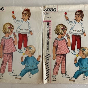 May include: Simplicity sewing pattern for a toddler outfit. The pattern includes two different styles: a red and white gingham top and pants, and a blue top and pants with a floral design. The pattern is for sizes 2 and 3.