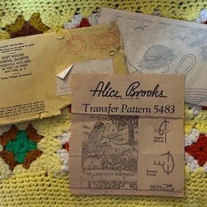 May include: A vintage Alice Brooks transfer pattern 5483 envelope and paper insert featuring a shepherd illustration and text, alongside a Fort Wayne Journal Gazette mailing envelope with a New York postmark, all printed on paper.