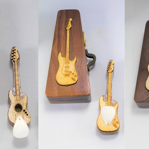 May include: Three wooden guitar cases with miniature guitars. The cases are made of dark wood and have a guitar design on the front. The guitars are made of light wood and have a natural finish.