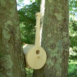 May include: A wooden birdhouse shaped like a banjo, mounted on a tree trunk. The birdhouse is painted in a natural wood color and has a round opening for birds to enter.