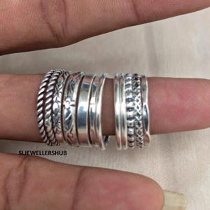 May include: A set of ten silver rings worn on a finger, featuring various textures including twisted rope, smooth polished bands, intricate floral engravings, beaded patterns, and geometric cross-hatch designs. The text SLJEWELLERSHUB is visible.