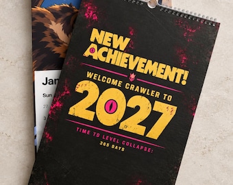 Può includere: Un calendario da parete con copertina nera e testo giallo che recita NEW ACHIEVEMENT! WELCOME CRAWLER TO 2027 TIME TO LEVEL COLLAPSE: 365 DAYS. Il design include accenti a spruzzo rosa e una rilegatura a spirale sul bordo superiore della carta.