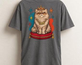 Può includere: Una t-shirt grigio antracite con la grafica di un gatto soffice che indossa una corona d'oro, occhiali tondi e una catena d'oro con la scritta Chonk. Il gatto è seduto su un cuscino rosso circondato da stelle e forme astratte.