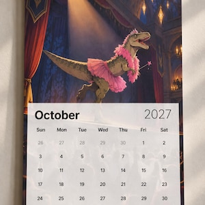 May include: A wall calendar for October 2027 featuring an illustration of a Tyrannosaurus rex wearing a pink tutu, a pink feather boa, and a small crown while holding a star-tipped wand on a stage with red curtains and warm lighting.