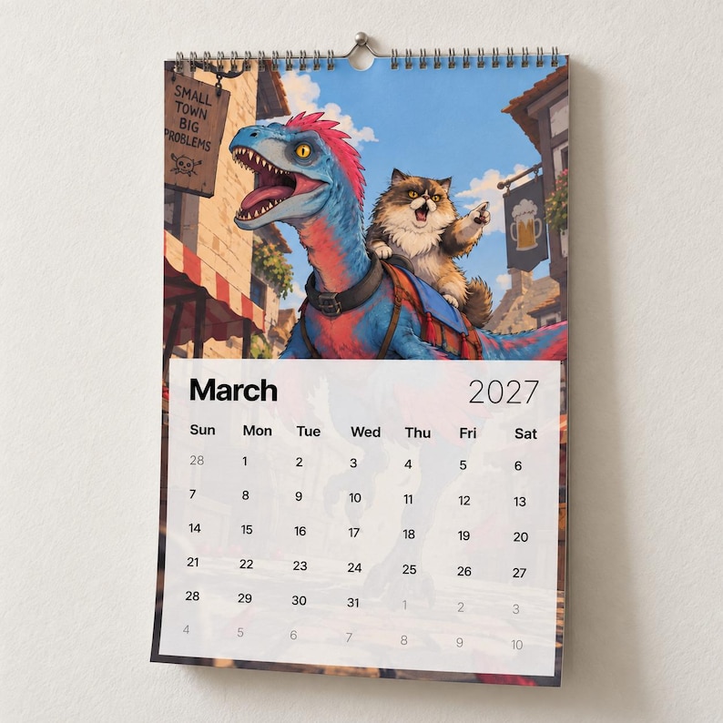May include: A wall calendar for March 2027 featuring an illustration of a blue and red dinosaur with a fluffy cat riding on its back. The scene includes a town background with a sign reading Small Town Big Problems and a beer mug icon sign.