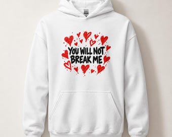 Può includere: Una felpa con cappuccio bianca caratterizzata da una grafica centrale con il testo nero "YOU WILL NOT BREAK ME" circondato da numerosi piccoli cuori rossi disegnati a mano e schizzi di vernice rossa sul petto.