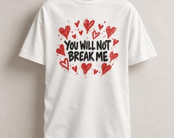 Può includere: Una t-shirt bianca a maniche corte con un design grafico centrale. Il testo "YOU WILL NOT BREAK ME" è stampato in grassetto nero, circondato da una disposizione circolare di cuori rossi disegnati a mano e schizzi di vernice.