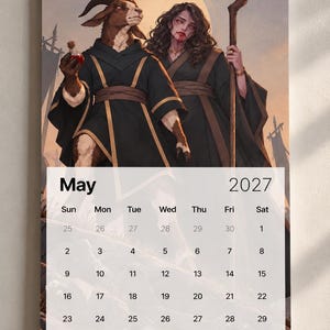 May include: A wall calendar for May 2027 featuring an illustration of a goat-headed figure in a black robe holding a red potion and a person with long dark hair holding a wooden staff, both set against a golden circular background.