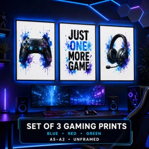 May include: A set of three rectangular wall art prints featuring a black gaming controller, the text "JUST ONE MORE GAME", and black gaming headphones. Each print has blue and purple watercolor paint splatters on a white background.