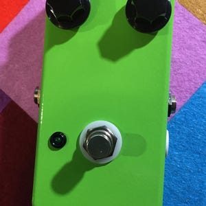 May include: Bright green rectangular effects pedal with two black knobs and a white footswitch. The pedal has a small green LED and two input/output jacks. The knobs have white indicator lines.