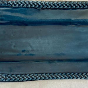 This is a handcrafted blue ceramic rectangular decorative tray featuring a textured braided rope border.  4 1/2 inch wide and 9 inch long.