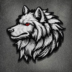 Könnte beinhalten: Ein gestickter Aufnäher mit dem Profil eines Wolfskopfes. Das Design verwendet weißes Garn für das Fell und die Gesichtszüge, das sich von einem schwarzen Hintergrund abhebt. Der Wolf hat ein einzelnes sichtbares Auge aus leuchtend rotem Garn.