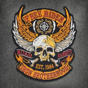 Pode incluir: Um emblema bordado preto com uma caveira branca central e asas laranja e brancas. O texto diz FREE RIDER no topo, ROAD KNIGHTS no meio e IRON BROTHERHOODS EST. 1984 na parte inferior. Um ícone de rosa dos ventos fica acima da caveira.