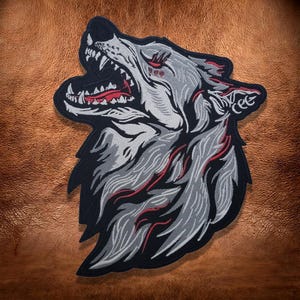 May include: An embroidered patch featuring a snarling wolf head in profile. The design uses shades of grey and white thread for the fur, with bold red accents highlighting the mouth, eyes, and fur texture, all outlined in a thick black border.