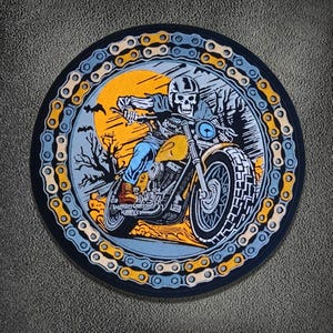Puede incluir: Un parche bordado circular que muestra un esqueleto con casco montando una motocicleta frente a un sol amarillo y árboles oscuros. El borde consiste en un patrón repetitivo de eslabones de cadena metálicos amarillos y azul claro.