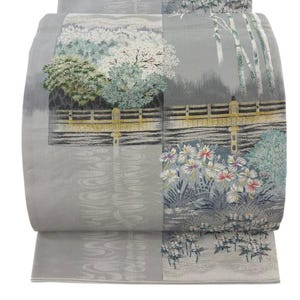 May include: A grey fabric panel featuring a woven landscape scene with a golden bridge, green trees, white flowers, and bamboo stalks. The design includes textured patterns of flowing water and foliage in shades of grey, white, green, and gold.