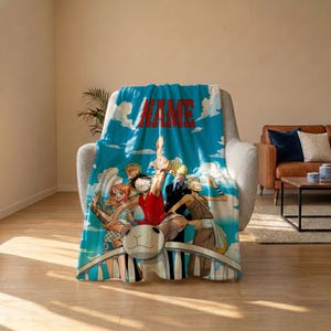 May include: A blue fleece blanket featuring a printed graphic of five anime characters from One Piece standing on a white railing against a sky background with clouds. The word NAME is printed in large red capital letters at the top center.