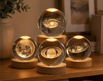 Peut inclure: Quatre sphères en verre transparent reposant sur des socles circulaires en bois. Chaque sphère contient un motif 3D gravé au laser : une galaxie spirale, la lune, la planète Saturne avec ses anneaux et un modèle du système solaire.