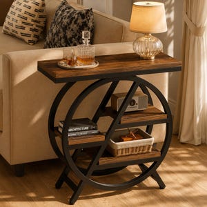 Peut inclure: Une table d'appoint dotée d'un cadre circulaire en métal noir et de trois étagères rectangulaires en bois. Le plateau supérieur supporte une carafe en verre, deux verres et une lampe. Les étagères inférieures contiennent un livre, une radio et un panier.