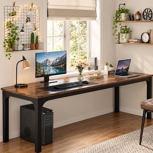Peut inclure: Un long bureau rectangulaire avec une surface en bois sombre et un cadre en métal noir. Le bureau comprend un écran d'ordinateur, un clavier noir, une souris, un ordinateur portable, une lampe de bureau et un vase de fleurs. Une tour noire est placée en dessous.