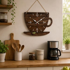 May include: A wall clock shaped like a coffee cup, crafted from dark brown wood planks with a visible grain. It features white numbers at 12, 3, 6, and 9, white clock hands, a red second hand, and a jute rope hanger. Decorative coffee beans and green leaves are attached.