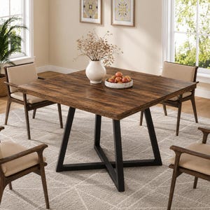 Peut inclure: Une table à manger carrée avec un plateau en grain de bois brun foncé et une base en métal noir en forme de X, entourée de quatre fauteuils à structure en bois foncé et assises beiges, avec un vase blanc et une coupe de fruits sur la table.