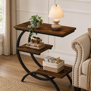 Peut inclure: Une table d'appoint en forme de C avec un cadre en métal noir et trois étagères en bois foncé. L'étagère supérieure porte une lampe beige et une plante en pot. L'étagère centrale porte deux livres et une figurine de rhinocéros dorée.
